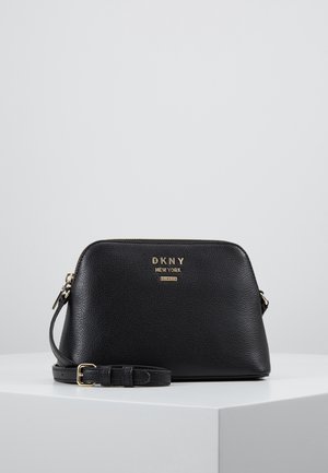 Bolso bandolera negro de cuero texturizado de DKNY con logotipo dorado y correa ajustable, exhibido sobre una superficie blanca contra un fondo liso.