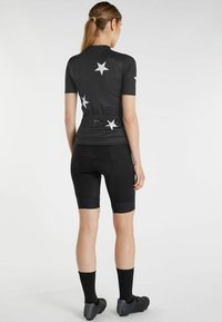 Zwart sportshirt met korte mouwen, voorzien van witte sterpatronen op de rug, gecombineerd met zwarte fietsshorts en donkere schoenen.