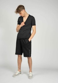 Sort v-hals t-shirt og mørke shorts med sidelommer med lynlås, der har en afslappet pasform og blød tekstur. Grå sko fuldender outfittet.