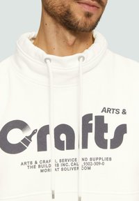Witte sweatshirt met hoge kraag, voorzien van een grote "Crafts" grafiek in donkergrijs en trekkoorden met zilverkleurige hardware.