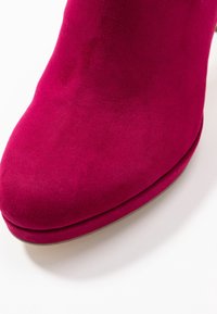 Botín de ante fucsia con punta redondeada, textura suave y un diseño elegante. Presenta un detalle de costura sutil cerca de la suela.