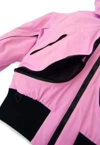 Rózsaszín dzseki fekete bordázott mandzsettákkal és szegéllyel, nyitott fekete cipzáras zsebbel és fekete első cipzárral, fehér háttéren.