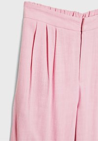 Pantalon rose taille haute avec plis à l'avant, une ceinture ornée d'un subtil détail volanté, et une fermeture éclair latérale dissimulée.