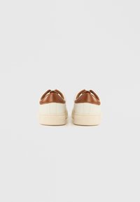 Para białych sneakersów niskoprofilowych z brązowymi akcentami na pięcie, widzianych od tyłu na jednolitym jasnym tle.