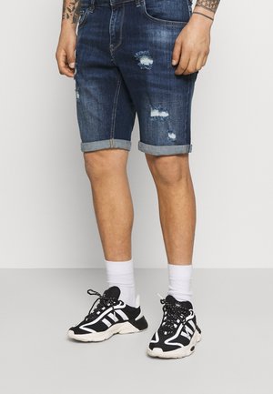 Shorts in denim scuri con dettagli strappati, orlo arrotolato, abbinati a sneakers bianche e nere e calzini bianchi alti.