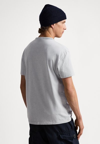 Grå bomullst-shirt med rund halsringning och korta ärmar, kombinerad med marinblå ribbad stickad mössa. Enkel design, minimal textur.