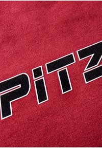 Red fabric with a textured surface featuring the word "PITZ" in black bold lettering outlined in white.
