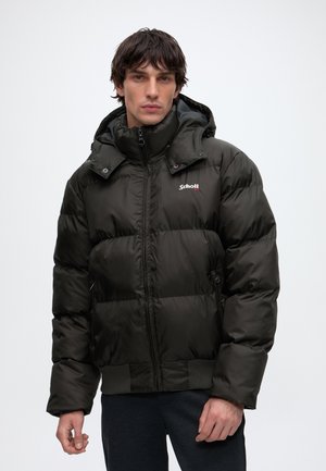 Homme portant une doudoune noire avec capuche, debout devant un fond clair uni, face à l'avant avec une expression neutre.