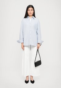 Light blue oversized button-up shirt with a chest pocket, paired with wide white pants and black pointed flats, holding a small black handbag.