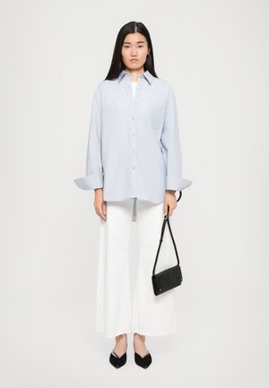 Light blue oversized button-up shirt with a chest pocket, paired with wide white pants and black pointed flats, holding a small black handbag.