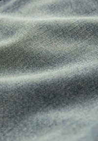 Gros plan sur un tissu en denim bleu clair montrant un tissage texturé et de doux plis.
