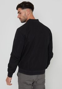 Schwarze Bomberjacke mit glatter Stoffoberfläche, gerippten Bündchen und Saum sowie einem minimalistischen Design. Verfügt über ein Logodetail am Ärmel.
