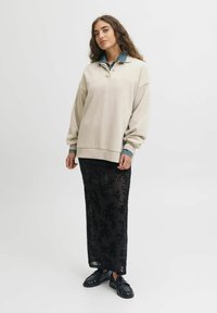 Beige oversized sweatshirt with denim collar, paired with a black sequined maxi skirt and black slip-on shoes, against a plain background.