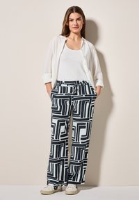 Mönstrade vida byxor i svart och vitt med geometriska mönster. Kombinerat med en vit skjorta och canvas sneakers.