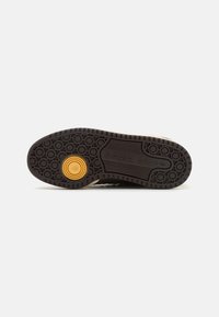 Brown rubber shoe sole with circular patterns and a yellow circular accent. Features textured grooves and "adidas" branding.