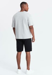 T-shirt di cotone grigio chiaro con vestibilità rilassata e colletto rotondo, abbinata a pantaloni corti neri a trama. Sneakers bianche completano il look.