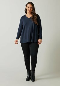 Maglia a maniche lunghe con scollo a V di colore navy con superficie testurizzata, abbinata a pantaloni skinny neri e stivaletti neri alla caviglia. Design semplice e dalla vestibilità rilassata.