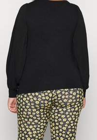 Top nero a maniche lunghe con maniche a sbuffo; abbinato a leggings aderenti con un motivo floreale giallo su uno sfondo scuro.
