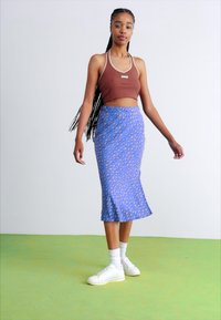 Fustă midi cu model albastru, cu o siluetă ajustată, asortată cu un top scurt maro și adidași albi, pe un fundal verde.