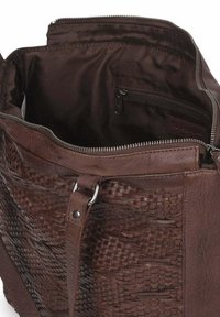 Bolso de cuero marrón con detalle tejido en la parte frontal, compartimento principal abierto que muestra un bolsillo interior con cremallera y forro de tela.