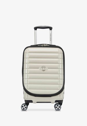 Harde koffer in crèmekleur met een ribbelpatroon, zwarte accenten, een uitschuifbare handgreep en vier draaiwielen voor mobiliteit.