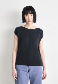 Top preto de manga curta com um corte descontraído, apresentando uma textura subtil. Combinado com jeans azul claro para um look casual.
