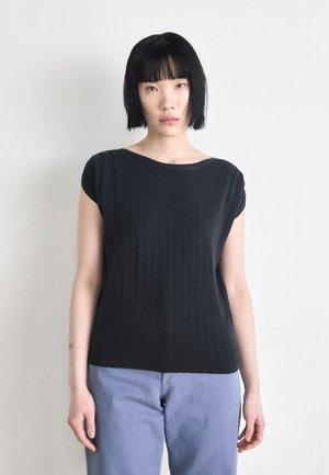 Black short-sleeve top with a relaxed fit, featuring a subtle texture. Paired with light blue jeans for a casual look.