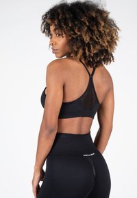 Sujetador deportivo negro con espalda de malla, que presenta tirantes delgados y un corte recto. Leggings negros de cintura alta con un logo en la cinturilla.