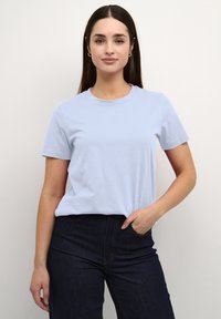 T-shirt en coton bleu clair à manches courtes et col rond, associé à un jean en denim foncé. Texture lisse, coupe décontractée.