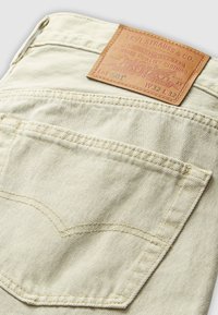 Beige Levi's 501 jeans back pocket with visible stitching and brown leather brand patch showing size W32 L32.