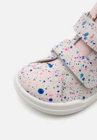 Velcro-Sneaker mit einem strukturierten, cremefarbenen Leder-Obermaterial, das mit pinken und blauen Spritzmustern verziert ist, einer weißen Gummisohle und einem weichen, rosa Innenfutter.