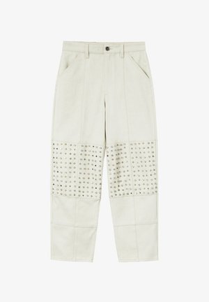 Pantaloni beige chiaro con una texture liscia, caratterizzati da borchie argento sui pannelli anteriori inferiori. Inclusi tasche frontali e chiusura con bottone.