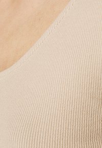 Beige geribbelde tanktop stof met een ronde halslijn en subtiele textuur; beschikt over een nette afwerking langs de randen.