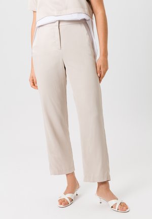 Helle beige weite Hosen aus glattem Stoff, mit einem einfachen Vorderfalten und Seitentaschen, kombiniert mit weißen Slipper-Sandalen.