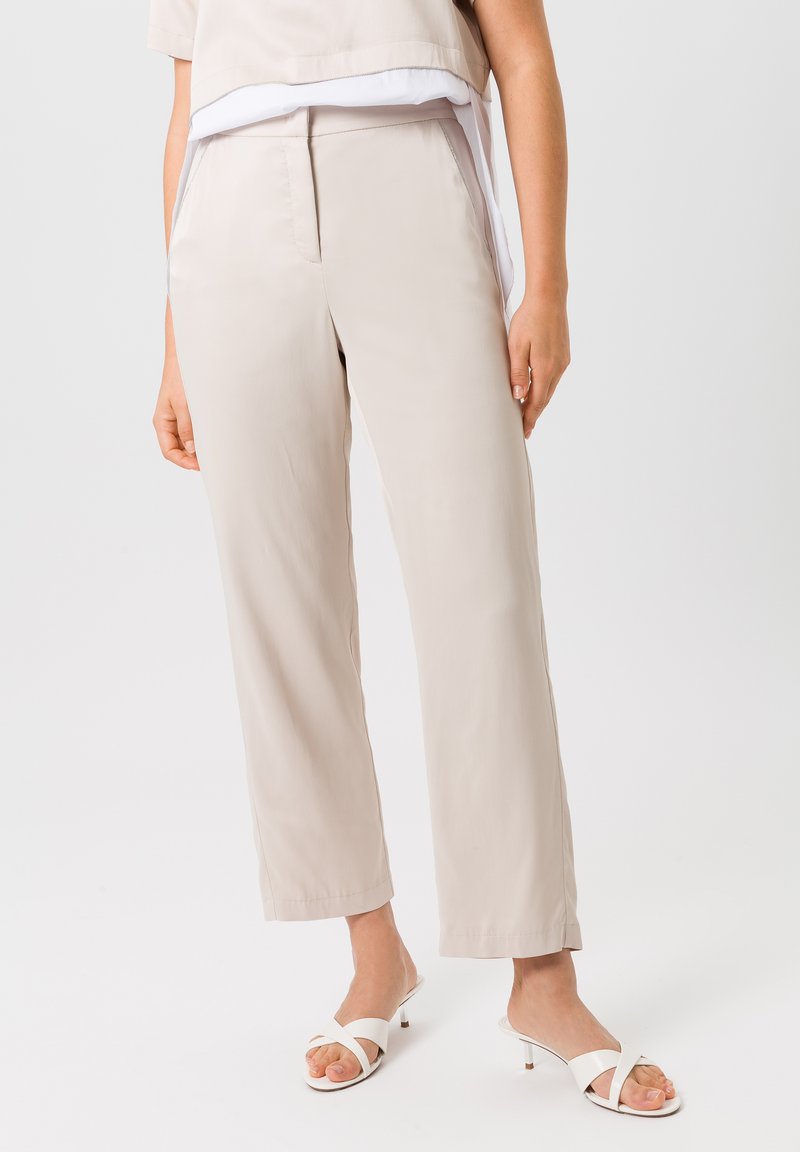 Lichtbeige brede broek gemaakt van een soepele stof, met een eenvoudige plooien aan de voorkant en zijzakken, gecombineerd met witte instappers.