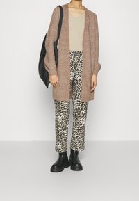 Lång, brun cardigan i en fluffig stickad kvalitet, tillsammans med en ljusbeige topp och leopardmönstrade vida byxor. Svarta kraftiga kängor och en tote-väska.