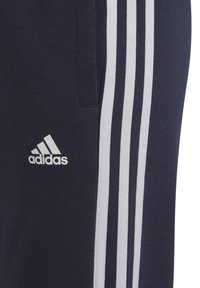Pantalones atléticos azul marino hechos de una tela suave, con tres rayas verticales blancas a lo largo del lado y un logo de Adidas en el muslo.