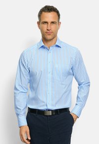 Camicia a strisce azzurro chiaro con maniche lunghe, pattina dei bottoni, colletto e tasca. Realizzata in un tessuto liscio, abbinata a pantaloni scuri.