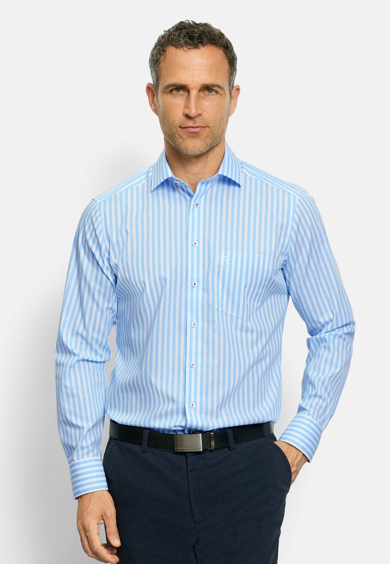 Camicia a strisce azzurro chiaro con maniche lunghe, pattina dei bottoni, colletto e tasca. Realizzata in un tessuto liscio, abbinata a pantaloni scuri.