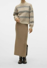 Pull beige à motifs avec des rayures bleues et noires, associé à une jupe longue en maille beige ajustée et des bottines marron.