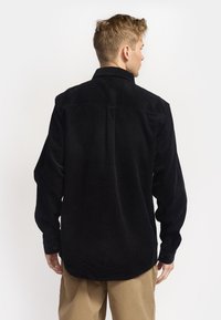 Zwarte corduroy overhemd met lange mouwen, een klassieke kraag en een rechte snit. Beschikt over een zichtbare ribbelstructuur en knoopsluitingen bij de manchetten.