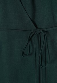 Tissu de robe enveloppante vert foncé avec une texture lisse, détail de taille nouée et léger éclat.