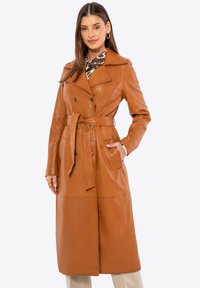 Abrigo trench de cuero color canela con diseño cruzado, cintura ceñida con cinturón, solapas grandes y bolsillos laterales, con una textura suave.