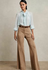 Hellblau, transparente Bluse mit gebundenem Ausschnitt; hellbraune, weite Hose mit Fronttaschen und sichtbaren Nähten; brauer Gürtel mit Metallschnalle.