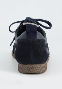 Granatowy tenisówka z zamszowym obcasem, materiałową pętelką, brązową gumową podeszwą z logo "pg" oraz sznurowadłami zawiązanymi na kokardę, widoczna od tyłu.