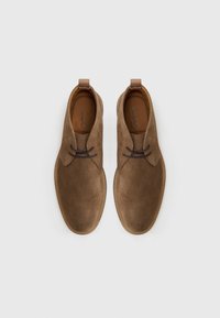 Botines de ante marrón con una textura suave, diseño de punta redonda y cordones marrones, presentando una plantilla beige con la marca "ALDO".
