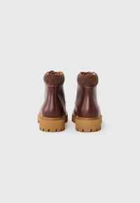 Botas de tobillo de cuero marrón con acentos de ante, una suela de goma gruesa con un profundo dibujo, y costuras visibles a lo largo de las uniones.