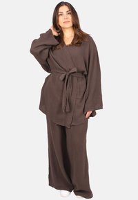 Braunes Baumwoll-Zweiteiler-Outfit mit einem langärmeligen Wickeloberteil mit Bindeband und weit geschnittenen Hosen, beide aus strukturiertem Stoff.