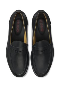 Zwarte leren instapschoenen met een gladde textuur, stiksels als accenten en een subtiel ontwerp op het voorblad, met een gele voering aan de binnenkant.