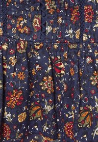 Tissu bleu foncé avec un motif floral en orange, rouge, jaune et vert, présentant des plis et une bordure en dentelle foncée.